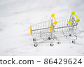 Shopping carts from supermarket on a light white background. Two empty stainless steel small miniature toy shopping trolley on marble table. Shopping concept. 86429624