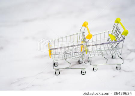 Shopping carts from supermarket on a light white background. Two empty stainless steel small miniature toy shopping trolley on marble table. Shopping concept. Shopping carts from supermarket on a light white background. Two empty stainless steel small miniature toy shopping trolley on marble table. Shopping concept. 86429624