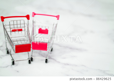 Shopping, purchases, supermarket, sale, mall concept. Two empty metal small miniature toy shopping trolley on light background. Selective focus. Shopping, purchases, supermarket, sale, mall concept. Two empty metal small miniature toy shopping trolley on light background. Selective focus. 86429625