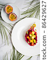 Flat lay of plates with mixed fruits and sliced fruits. Tropical fruit salad served in half dragon fruit. Dragon fruit, maracuja, papaya, palm leaves on table. Top view. 86429627