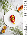 Flat lay of plates with mixed fruits and sliced fruits. Tropical fruit salad served in half dragon fruit. Dragon fruit, maracuja, papaya, palm leaves on table. Top view. 86429628