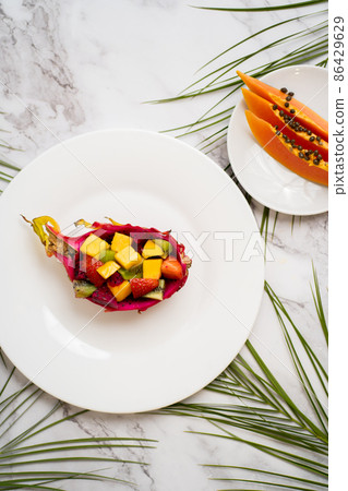 Tropical fruit salad served in half dragon fruit. Top view. Summer salad on white plate on table. Healthy breakfast, food concept. Flat lay. Vertical shot. Tropical fruit salad served in half dragon fruit. Top view. Summer salad on white plate on table. Healthy breakfast, food concept. Flat lay. Vertical shot. 86429629