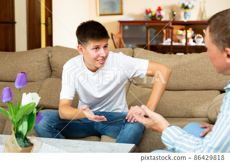Portrait of teen boy and his father chatting at sofa 86429818