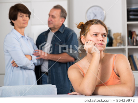 Upset female is sitting at the table and her parents are sympathying with her Upset female is sitting at the table and her parents are sympathying with her 86429978
