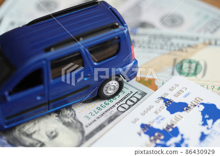 Blue toy car standing on dollar bills and plastic credit card closeup Blue toy car standing on dollar bills and plastic credit card closeup 86430929