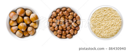 Hazelnuts in white bowls. Whole, dried nuts of Corylus avellana, with and without shells, ready to eat as snack, and ground nuts, used for baking. Isolated from above, on white background, food photo. 86430940