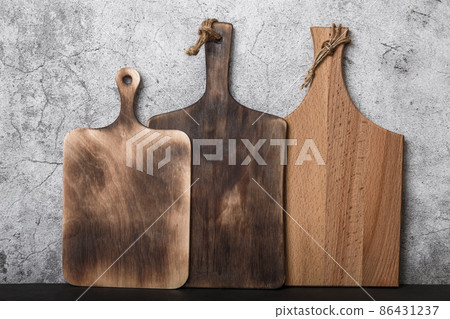 Samples of three different rustic wooden cutting boards on a kitchen countertop against a concrete wall. Manufacture of household goods and accessories made of wood 86431237