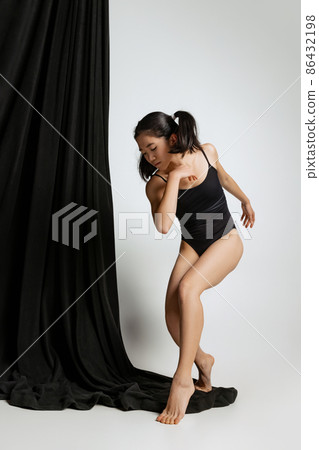 Full-length studio portrait of beautiful slim woman in bodysuit dancing, posing isolated over gray background Full-length studio portrait of beautiful slim woman in bodysuit dancing, posing isolated over gray background 86432198
