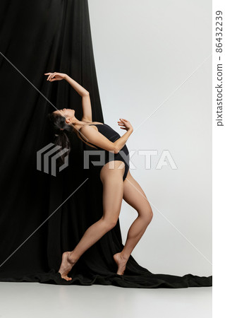 Full-length portrait of young woman posing in bodysuit isolated over gray studio backgrounf with black portiere Full-length portrait of young woman posing in bodysuit isolated over gray studio backgrounf with black portiere 86432239