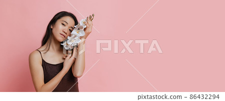 Beautiful young woman in brown bodysuit with tender white orchid flower posing isolated over pink studio background. Flyer 86432294