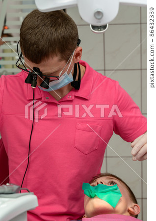The dentist installs a rubber dam and a clamp for the treatment of a diseased tooth. The dentist installs a rubber dam and a clamp for the treatment of a diseased tooth. 86432339