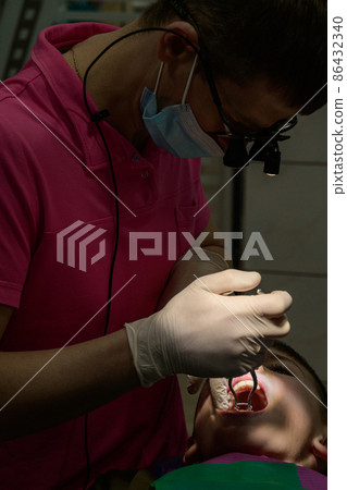 The pediatric dentist treats the child's teeth, brushing the tooth from caries with a drill. 86432340