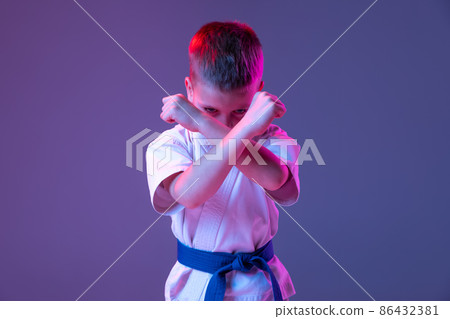 Dynamic portrait of kid, young male taekwondo, karate athletes in doboks doing basic movements isolated on purple background in neon. Concept of sport, martial arts Dynamic portrait of kid, young male taekwondo, karate athletes in doboks doing basic movements isolated on purple background in neon. Concept of sport, martial arts 86432381