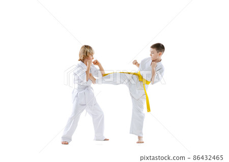 Dynamic portrait of two little boys, taekwondo or karate athletes wearing doboks training together isolated on white background. Concept of sport, martial arts Dynamic portrait of two little boys, taekwondo or karate athletes wearing doboks training together isolated on white background. Concept of sport, martial arts 86432465