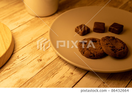 Chocolate chip cookies on a plate and chocolates, cups, table lamps Chocolate chip cookies on a plate and chocolates, cups, table lamps 86432664
