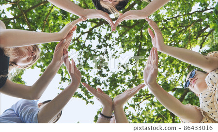 A group of girls makes a heart shape from their hands against the background of tree branches. A group of girls makes a heart shape from their hands against the background of tree branches. 86433016