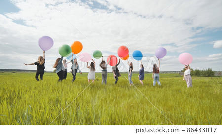 Cheerful girls are standing on the field with large balloons and colorful balloons. Cheerful girls are standing on the field with large balloons and colorful balloons. 86433017