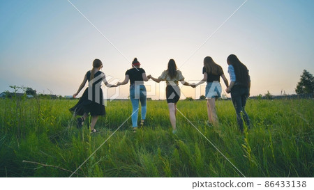 Girls friends go hand in hand at sunset across the field. Girls friends go hand in hand at sunset across the field. 86433138