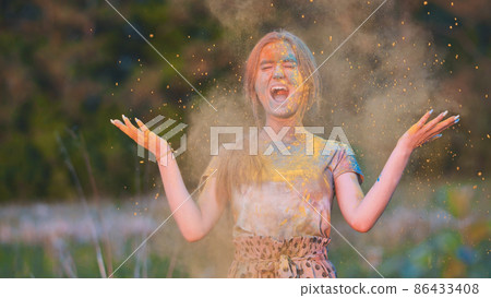 Friends sprinkle their cheerful girlfriend with multi-colored powder. Holi holiday. 86433408