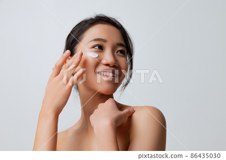 Cropped portrait of young smiling woman doing skincare routine, moisturizing face with special cream Cropped portrait of young smiling woman doing skincare routine, moisturizing face with special cream 86435030