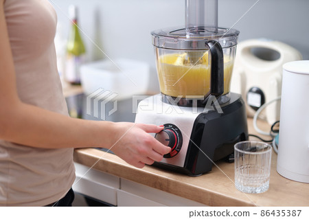Woman cook turning on button of food processor for kneading dough closeup Woman cook turning on button of food processor for kneading dough closeup 86435387