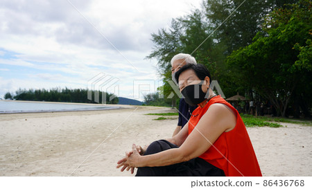 Asian senior couple with mask relax sitting on beach log white sand landscape and beautiful sea Asian senior couple with mask relax sitting on beach log white sand landscape and beautiful sea 86436768