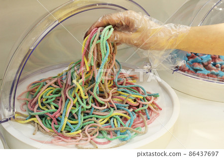 a girl in a disposable glove types chewing marmalade strips of worms.Close-up, the use of disposable gloves protective equipment compliance with sanitary standards a girl in a disposable glove types chewing marmalade strips of worms.Close-up, the use of disposable gloves protective equipment compliance with sanitary standards 86437697