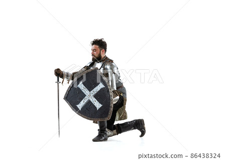Portrait of serious manm medieval warrior, knight in special protective covering sitting on one knee isolated over white background Portrait of serious manm medieval warrior, knight in special protective covering sitting on one knee isolated over white background 86438324