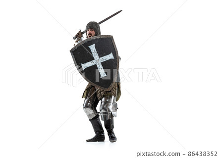 Portrait of brutal serious man, medieval warrior or knight in protective covering with sword preparing to attack isolated over white studio background Portrait of brutal serious man, medieval warrior or knight in protective covering with sword preparing to attack isolated over white studio background 86438352