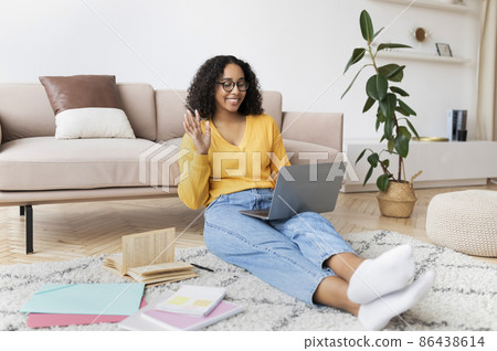 Black lady with study materials making video call on laptop, waving at webcam, participating in remote class from home Black lady with study materials making video call on laptop, waving at webcam, participating in remote class from home 86438614