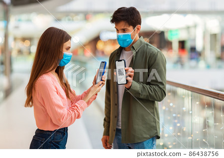 Couple Showing Phones With QR Codes Wearing Masks In Hypermarket Couple Showing Phones With QR Codes Wearing Masks In Hypermarket 86438756
