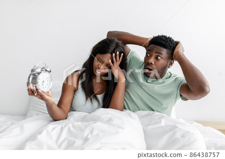 Sad dissatisfied sleepy millennial black lady and man sitting on white bed in bedroom hold heads with hands Sad dissatisfied sleepy millennial black lady and man sitting on white bed in bedroom hold heads with hands 86438757