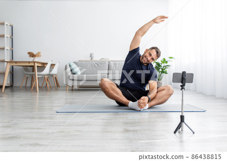 Cheerful millennial muscular caucasian guy in uniform sitting on floor on mat in lotus position, practicing yoga Cheerful millennial muscular caucasian guy in uniform sitting on floor on mat in lotus position, practicing yoga 86438815