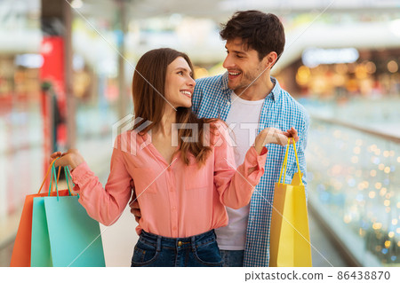 Husband Hugging Wife Holding Shopping Bags Buying Clothes In Mall Husband Hugging Wife Holding Shopping Bags Buying Clothes In Mall 86438870