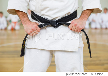 Karate master in a white kimono and with a black belt, stands in front of the formation of his students. Martial arts school in training in the gym. 86439540