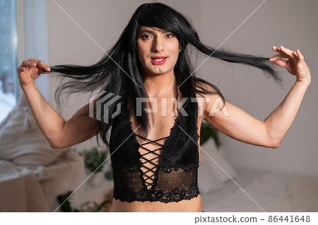 A homosexual guy in black lace underwear and a wig grimaces at the camera. A homosexual guy in black lace underwear and a wig grimaces at the camera. 86441648
