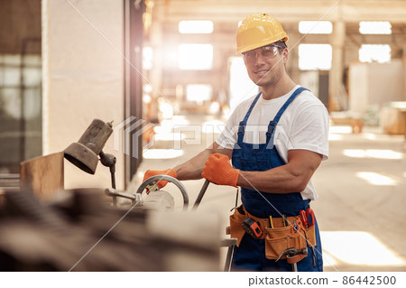 Cheerful male builder using professional equipment in workshop 86442500