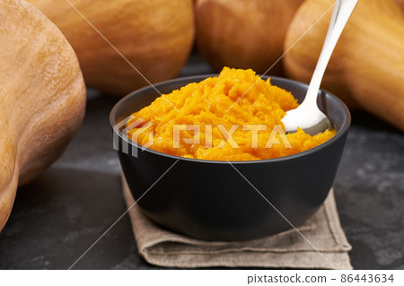 Bowl of homemade puree with organic pumpkin butternut squash on a black stone table, selective focus. 86443634