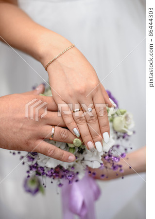 hands with wedding rings over a bouquet of flowers in shallow depth of field 86444303