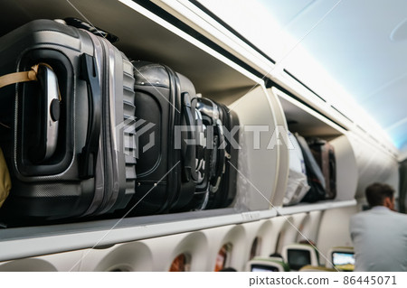 Airplane overhead locker with black plastic baggage suitcases, closeup detail Airplane overhead locker with black plastic baggage suitcases, closeup detail 86445071