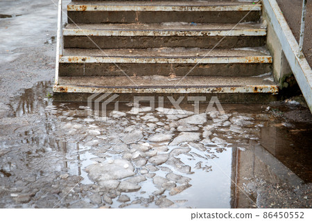 Dangerous and unsafe stairs. Melted snow, water and slippery. Concrete and rusty metal 86450552