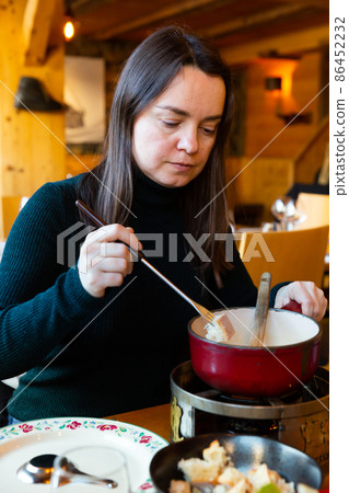 Woman eating fondue with piece of bread and special fork Woman eating fondue with piece of bread and special fork 86452232