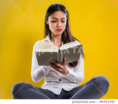 Young woman reading a book - studio shot against yellow background Young woman reading a book - studio shot against yellow background 86452482