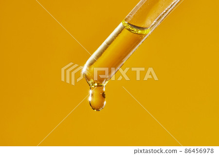 A drop of cosmetic aromatic oil drips from the pipette. Front view. A drop of cosmetic aromatic oil drips from the pipette. Front view. 86456978