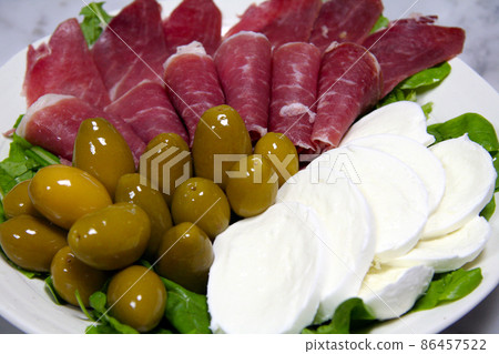 Prosciutto ham, mozzarella cheese and green olives on a white plate. 86457522
