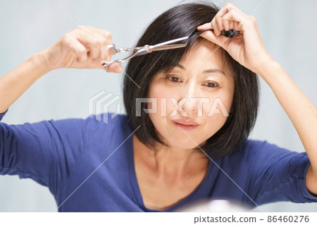 Middle-aged female who self-cuts Middle-aged female who cuts her bangs with scissors Upper body 86460276