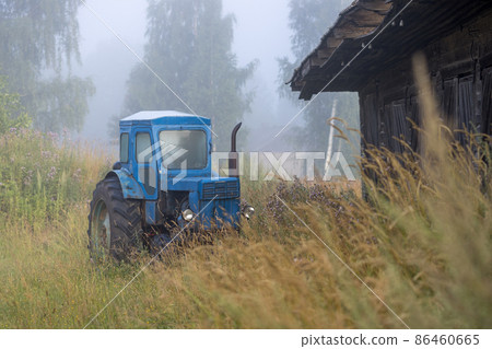An old blue agricultural tractor in the tall grass on the outskirts of the village 86460665