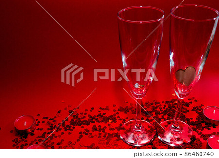 Glasses of champagne, red candles, red confetti in the shape of a heart on a red background Glasses of champagne, red candles, red confetti in the shape of a heart on a red background 86460740