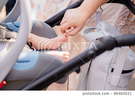 a woman's hand touches a leg of a little boy sleeps strapped in a stroller. a woman's hand touches a leg of a little boy sleeps strapped in a stroller. 86460831