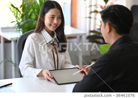 Cheerful businesswoman holding digital tablet and working with her colleague. Cheerful businesswoman holding digital tablet and working with her colleague. 86461076